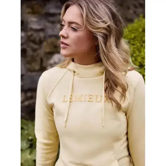 A pale yellow lemieux martha hoodie mimosa with long sleeves high collar and gold embroidered logo on chest