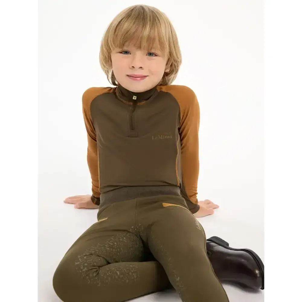A child wearing a brown and tan lemieux mini base layer alpine top with olive green breeches for mini riders running