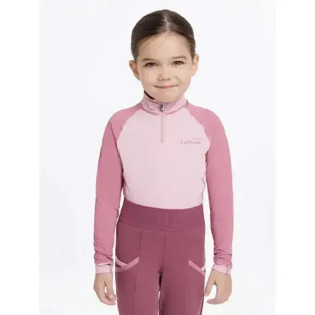 A child wearing lemieux mini base layer blossom in pink and mauve with a half-zip long sleeve top and matching leggings