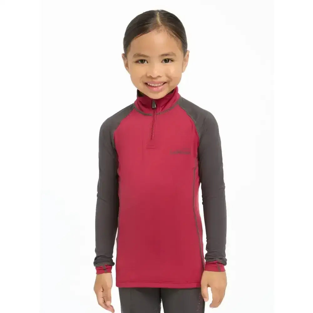 A child wearing a red and gray lemieux mini base layer ember with a half zip collar perfect for mini riders running