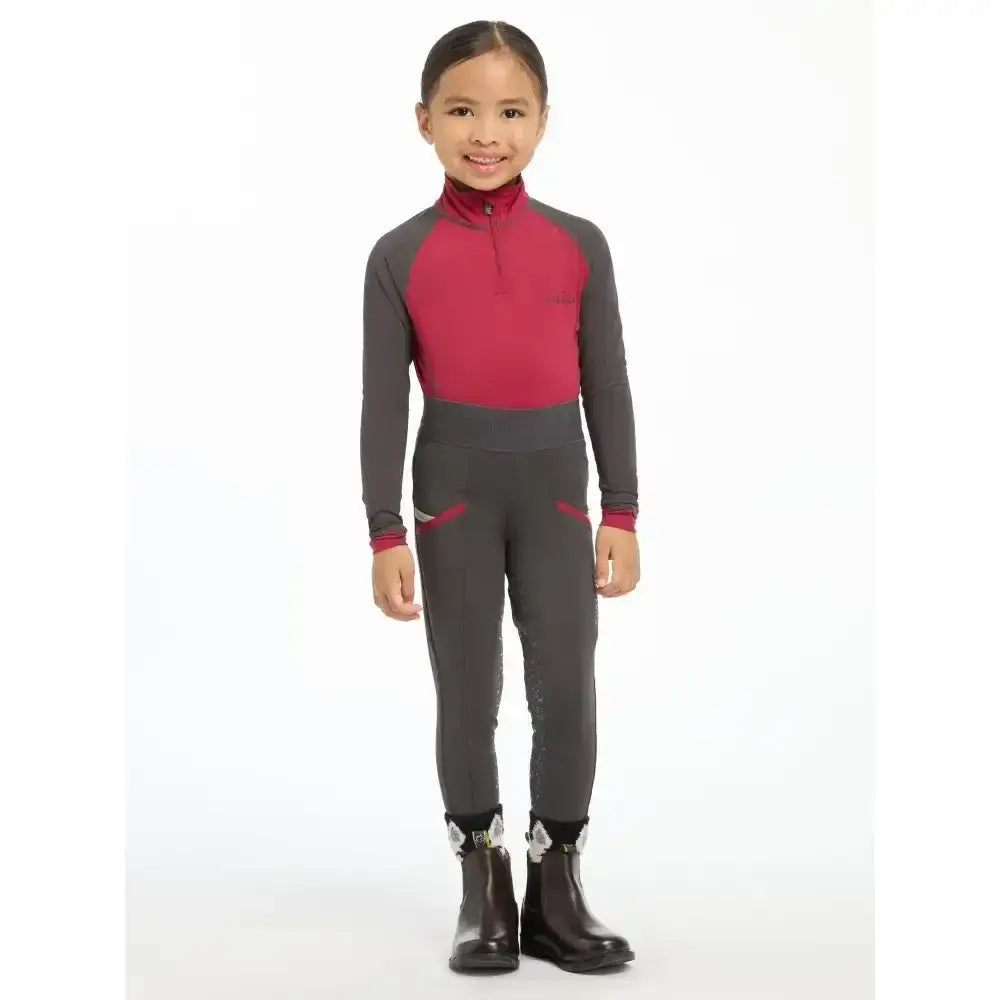 A child wearing a lemieux mini base layer ember suit with a magenta torso and gray sleeves perfect for mini riders running