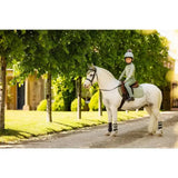 A young rider wearing the lemieux mini base layer fern in light green sits on a white horse on a sunny path