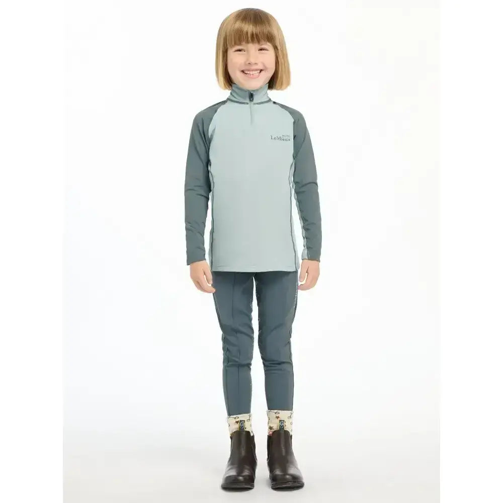 A child wearing a lemieux mini base layer glacier in light blue and dark gray with a quarter-zip collar and matching pants