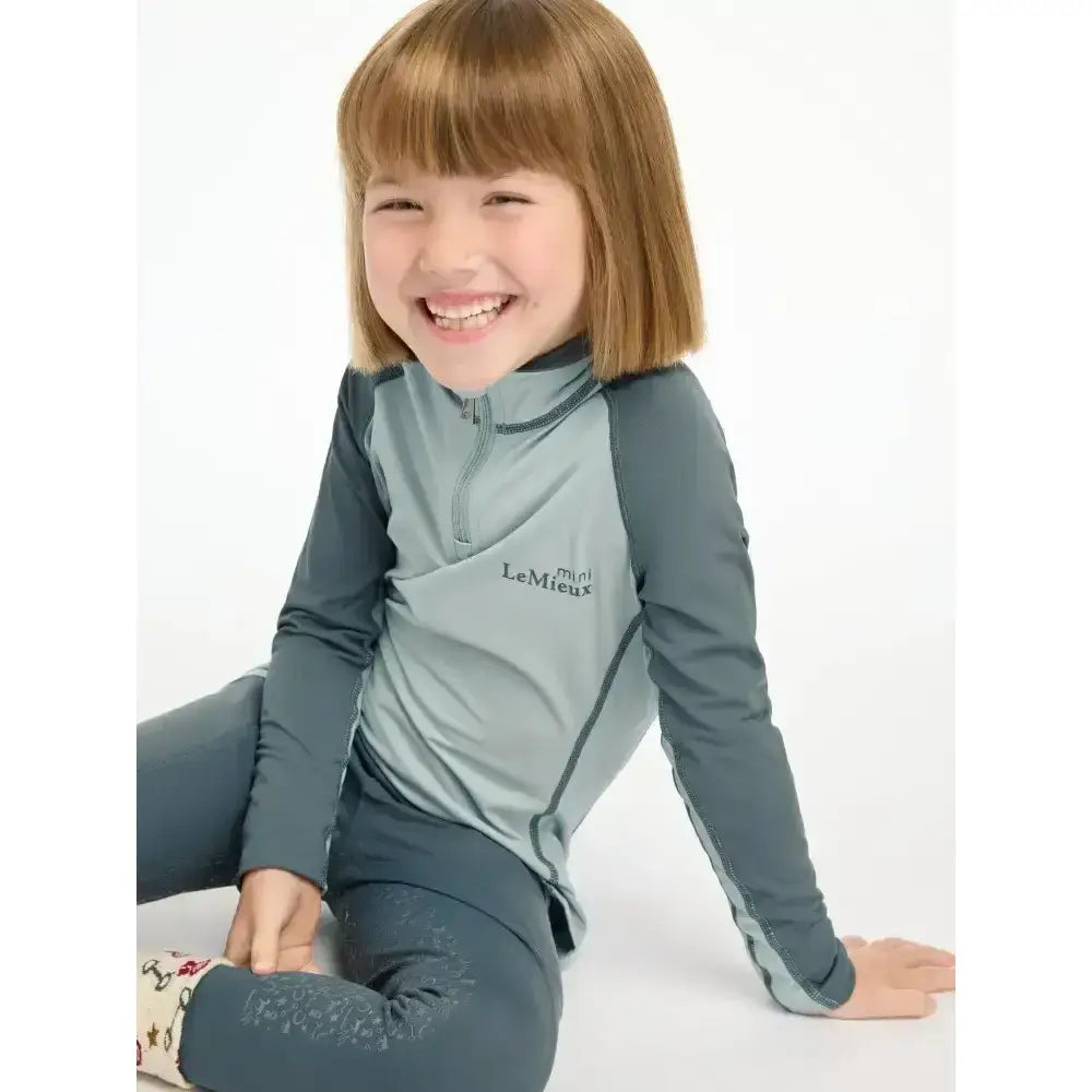 A child wearing a lemieux mini base long-sleeved glacier base layer with matching leggings for mini riders running