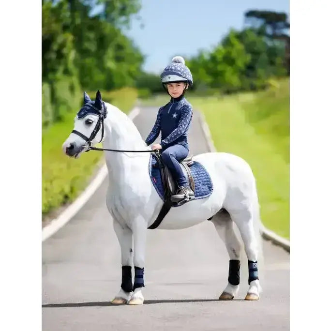 Young rider on white horse wearing navy blue lemieux mini base indigo matching protective gear and tack