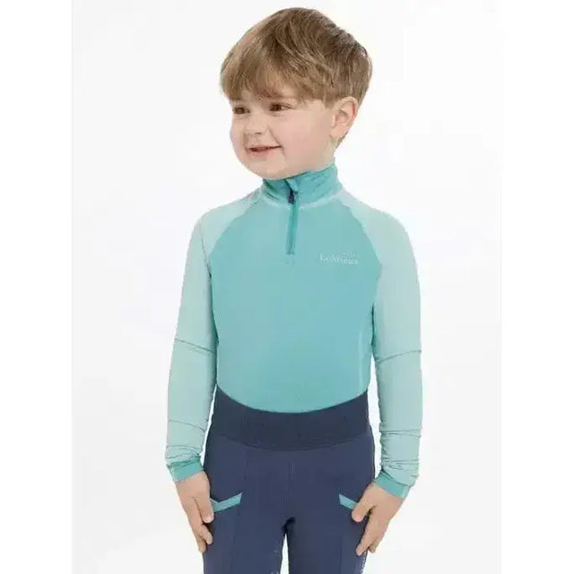 A child wearing a teal and navy lemieux mini base layer lagoon long-sleeve athletic top with quarter-zip collar