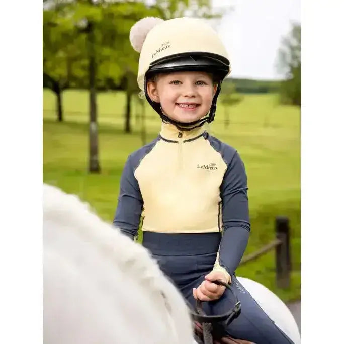 Cream-colored lemieux mini base layer mimosa equestrian helmet with fluffy white pom-pom on top