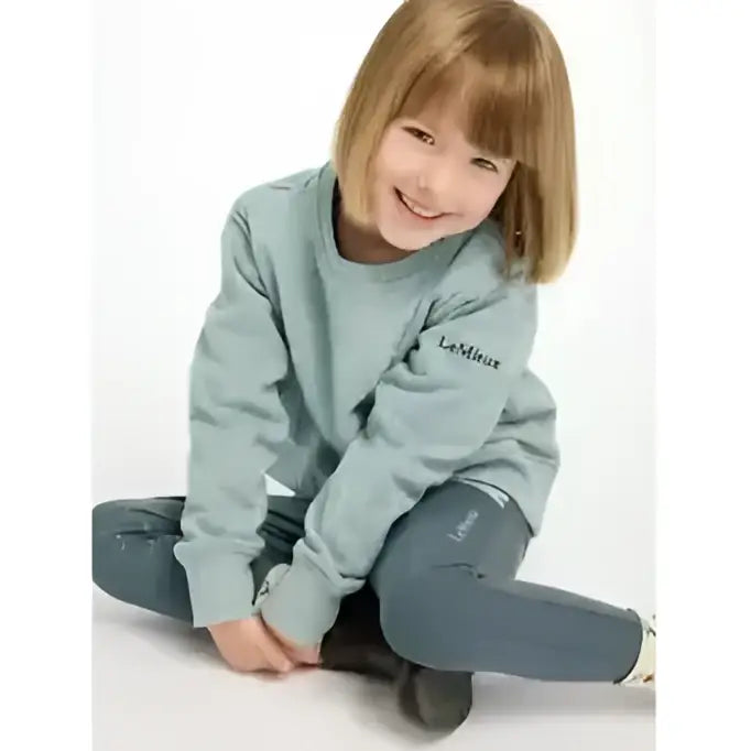 A young child wearing a light blue lemieux mini casey crew sweatshirt with brand embroidery on the chest