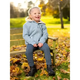 A young girl wearing a lemieux mini charlie super snuggly lined hoodie glacier sits on a wooden bench