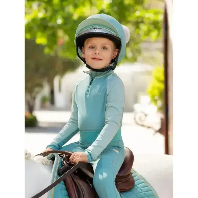 A child wearing a lemieux mini double pom double pom hat in silk lagoon with matching riding clothes