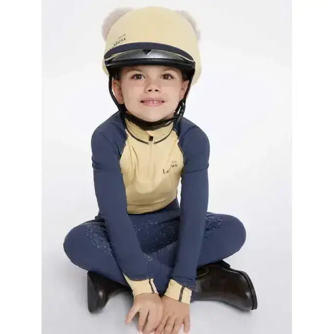 Child wearing a beige and navy blue lemieux mini double pom hat silk mimosa equestrian helmet with black trim