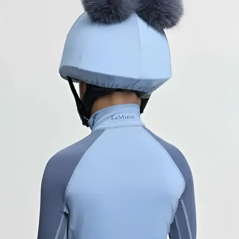 Light blue lemieux mini double pom equestrian helmet cover in silk powder blue with two gray fluffy pom-poms on top