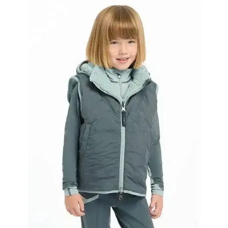 A child wearing a dark gray lemieux mini elsie reversible gilet petrol with light blue sherpa-lined hood and zipper accents