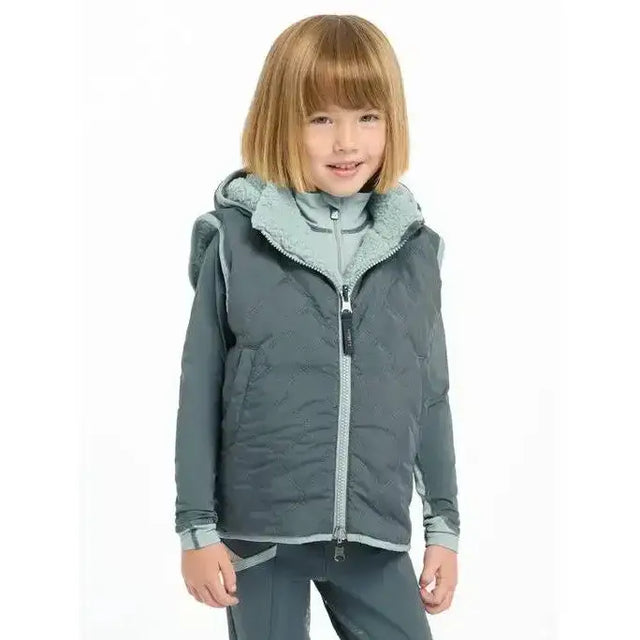 A child wearing a dark gray lemieux mini elsie reversible gilet petrol with light blue sherpa-lined hood and zipper accents