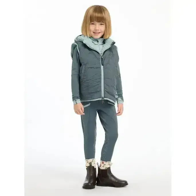 A child models a lemieux mini elsie reversible gilet petrol quilted dark teal vest with a blue hood and matching leggings