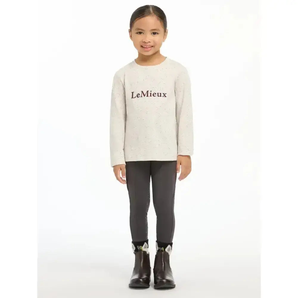 A child wearing a soft ecru lemieux mini jessie long sleeve top with black lemieux lettering across the chest