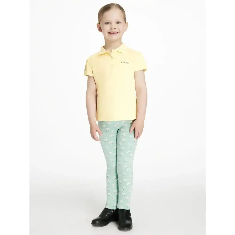 A child wearing lemieux mini leggings in light green with white hearts and a pale yellow polo shirt with brand logo