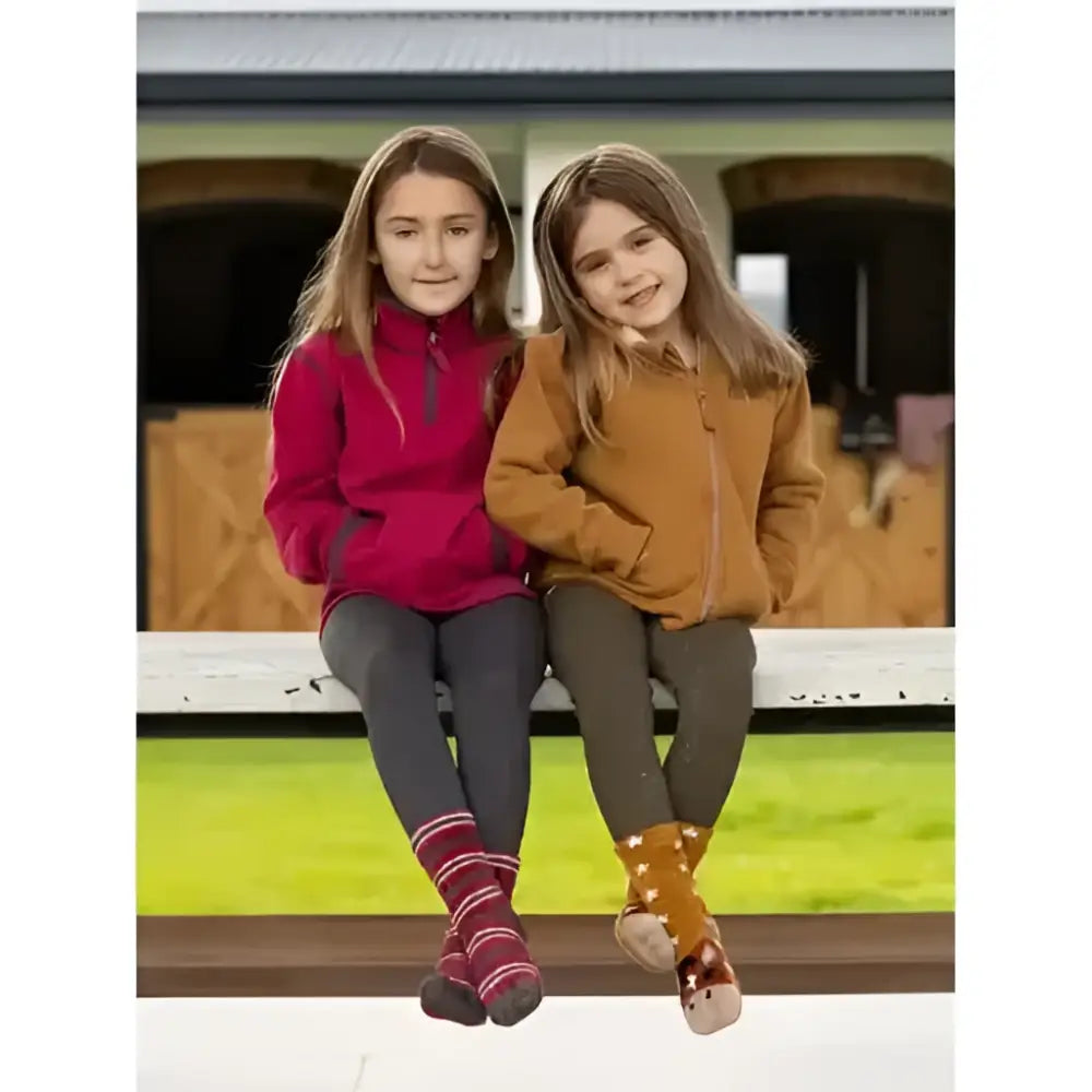 Two kids sit on a bench wearing lemieux mini mari micro fleece ember jackets in red and brown fleece material