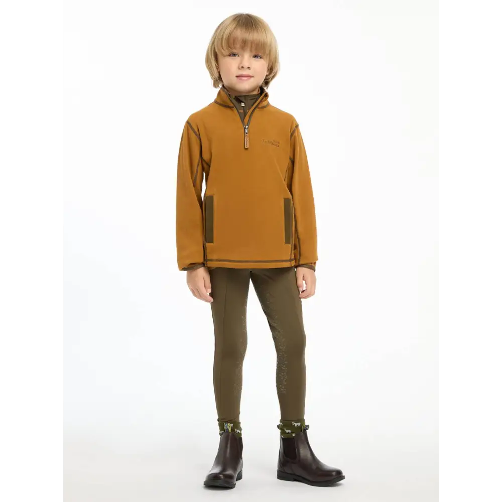 Child in Lemieux Mini Mari Micro Fleece Ginger pullover, brown pants, and black boots