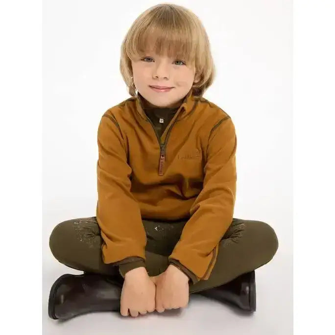 A young boy wearing a lemieux mini mari micro fleece ginger jacket in mustard yellow with dark green pants and black boots