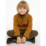 A young boy wearing a lemieux mini mari micro fleece ginger jacket in mustard yellow with dark green pants and black boots