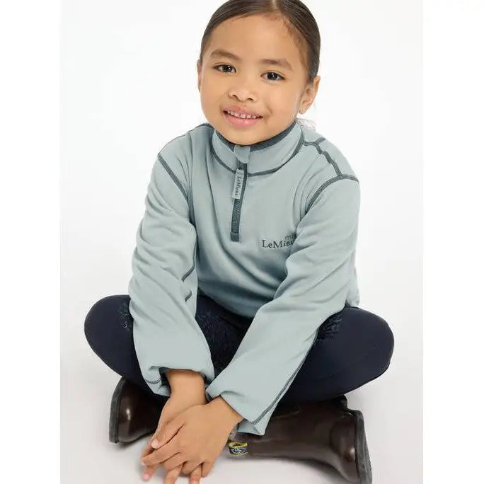 Smiling child in Lemieux Mini Mari Micro Fleece Glacier sweater and dark pants