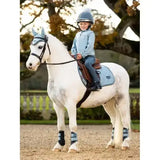 A young rider wears a lemieux mini mari micro fleece glacier jacket while sitting on a white horse with matching blue gear