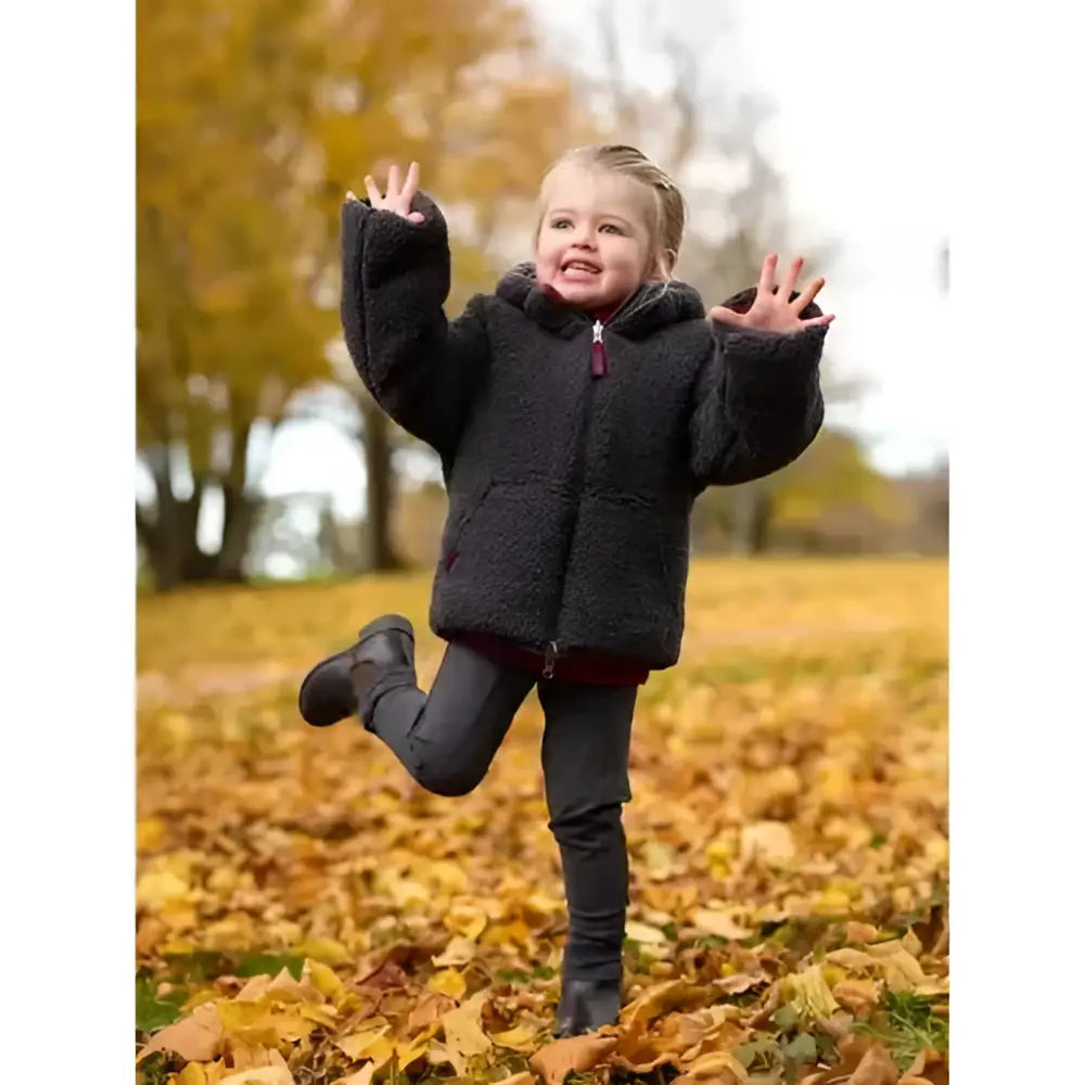 A child wearing a black fluffy shearling lemieux mini megan reversible puffer ember coat with hood and zipper closure