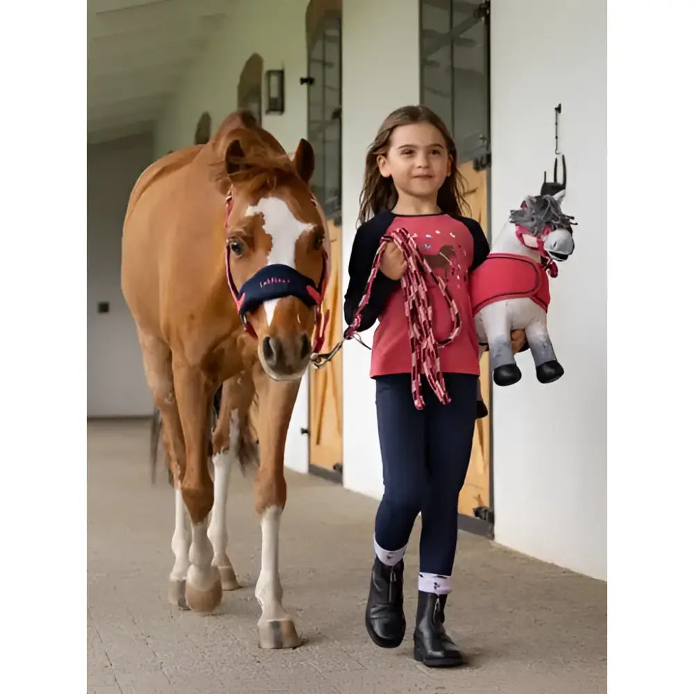 A young girl holds a plush toy horse wearing a lemieux mini nora brushed pull on navy top with pink and black details