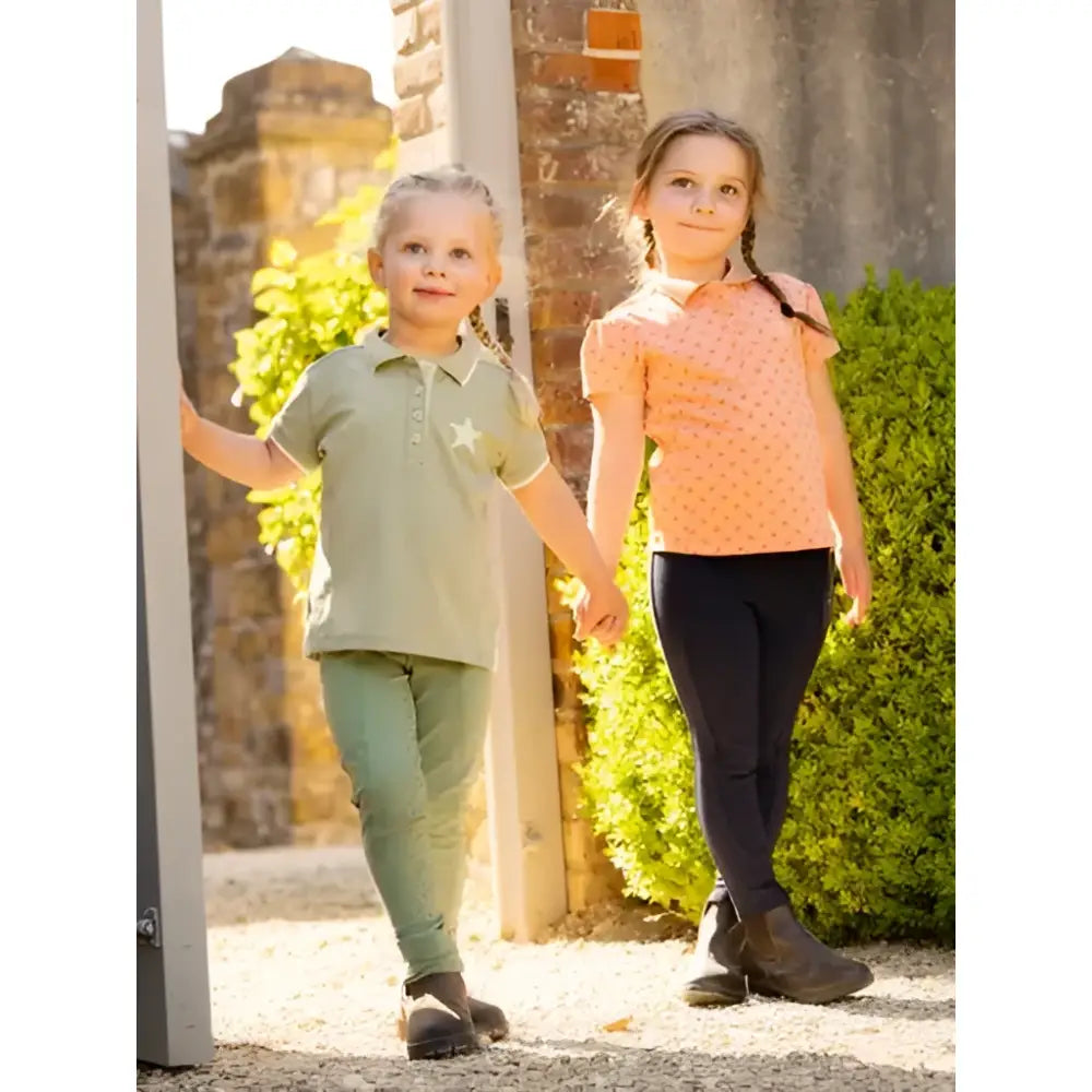 Two young girls wearing lemieux mini polo shirt fern in soft pique jersey in light green and orange polka-dot designs