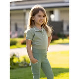 A young girl wearing a lemieux mini polo soft pique jersey shirt fern in light green with white trim and matching pants