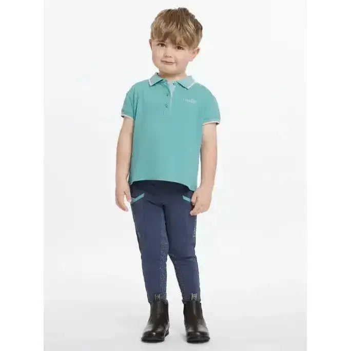 A child wearing a lemieux mini polo shirt lagoon teal with star buttons and matching navy riding pants with patterned accents