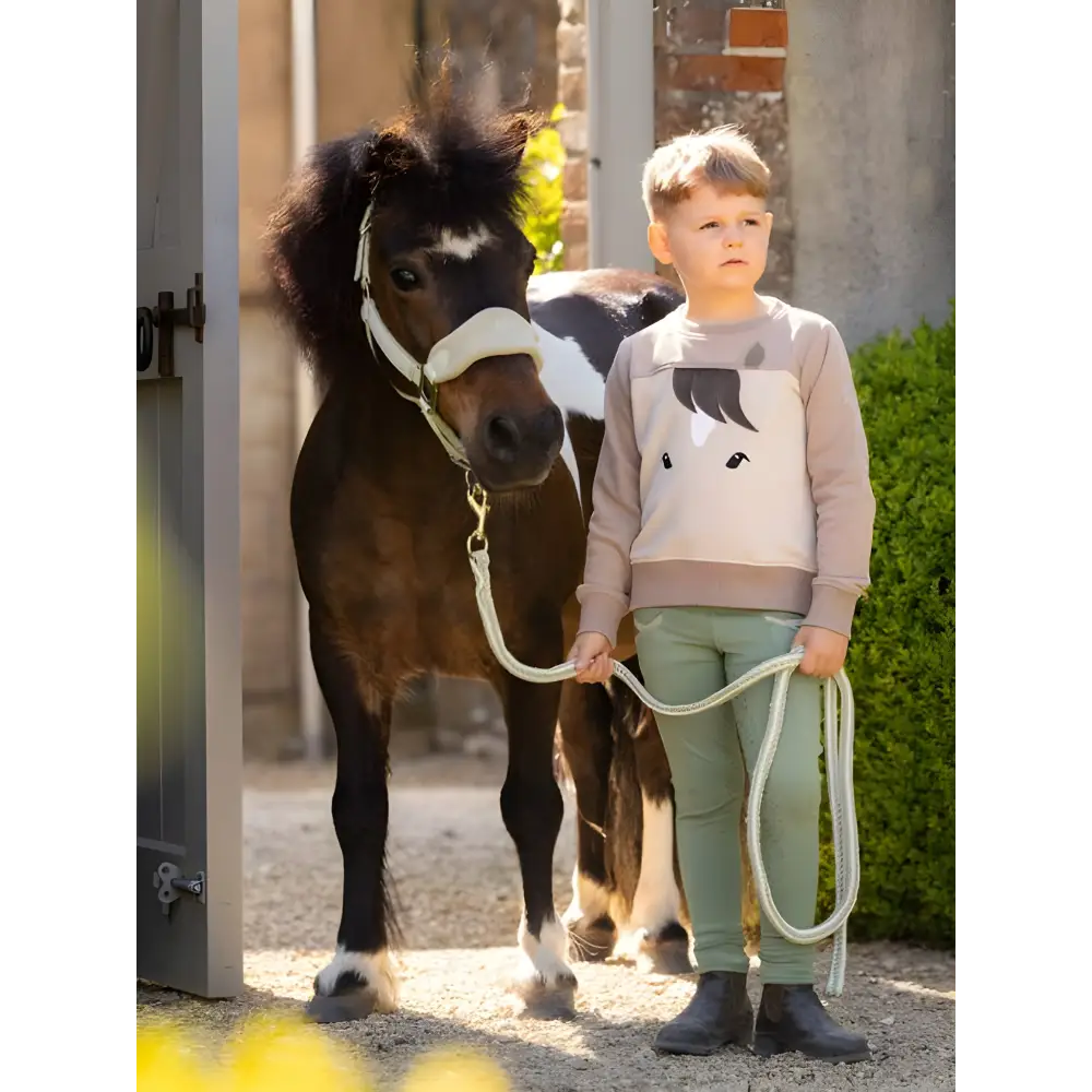 Child beside a small pony wearing a Lemieux Mini Pony Sweatshirt in Stone color