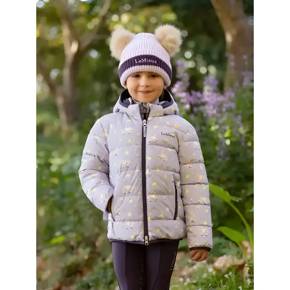 A child wearing a lemieux mini printed lilo puffer jacket lilac with floral pattern and matching knit hat with pom poms