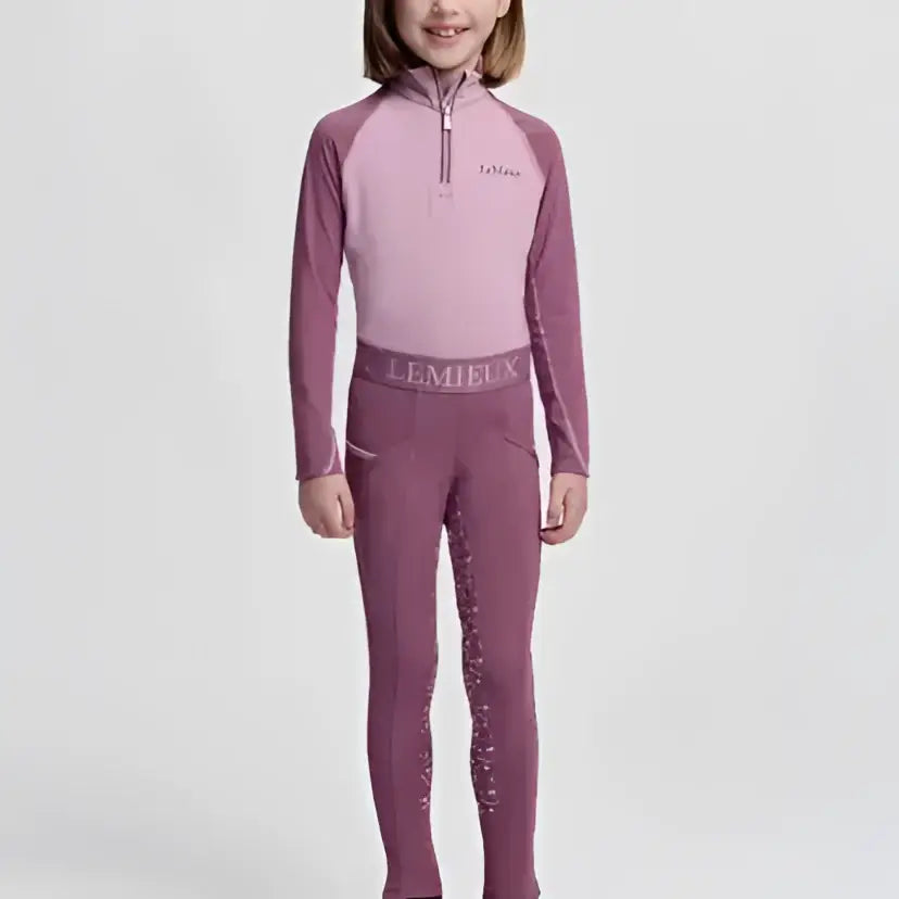 A young girl wearing a lemieux mini pull breech mallow in two-tone purple with 4-way stretch glitter accents