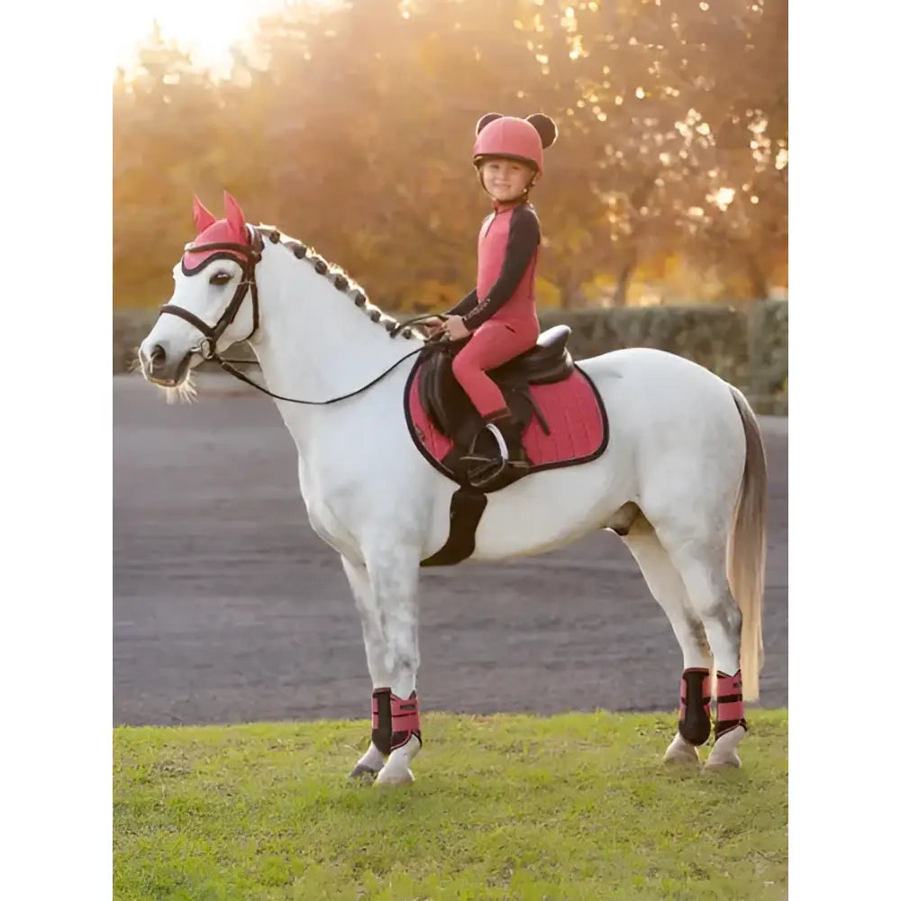 A young girl in pink riding gear sits on a white horse wearing red lemieux mini pull ons cranberry boots