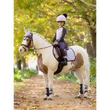 A young rider in a white helmet rides a pinto horse wearing lemieux mini pull ons juniper protective leg wraps