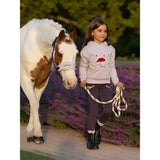 A young girl in a lemieux mini romi lilac hoodie with floral embroidery walks beside a white and brown horse