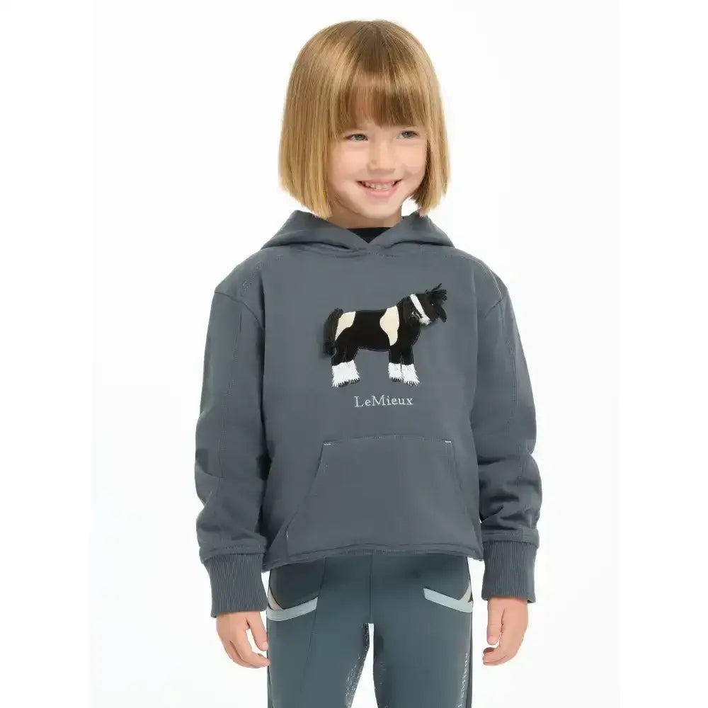A child wearing a lemieux mini romi hoodie petrol in dark gray with a black and white embroidered horse design on front