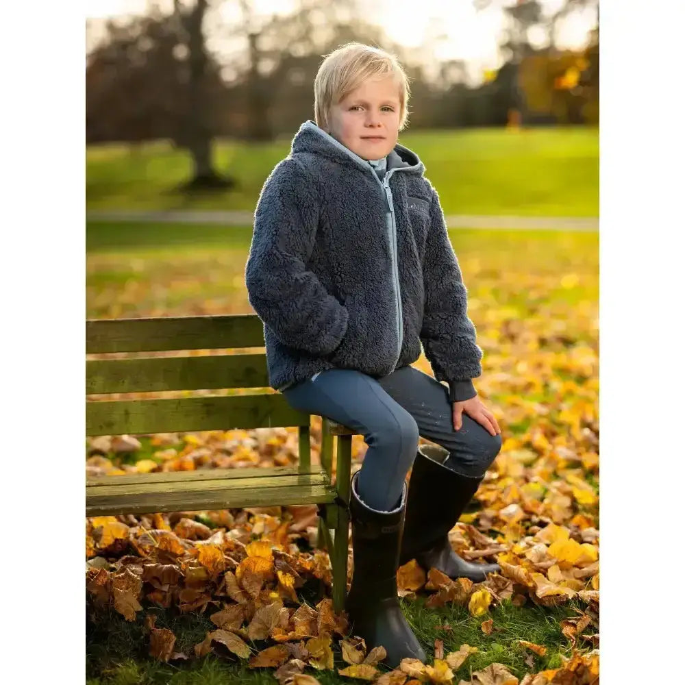 A child wearing a lemieux mini teagan fleece petrol navy blue hooded jacket with light gray trim and zipper