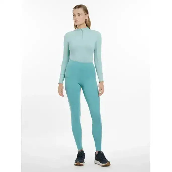 A woman wears a lemieux naomi pull two-piece athletic set in soft teal with long sleeves and high-waisted leggings