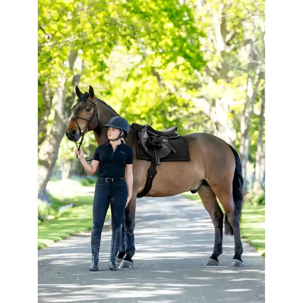 Brown horse with rider wearing equestrian gear standing next to lemieux pillow pad black on saddle black bridle
