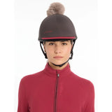 Dark gray lemieux pom hat silk cinder equestrian helmet with pink trim and a fluffy brown pom-pom made from silky smooth four-way fabric