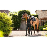 A dark brown horse jumps wearing a lemieux puissance suede close contact square black saddle pad with bridle