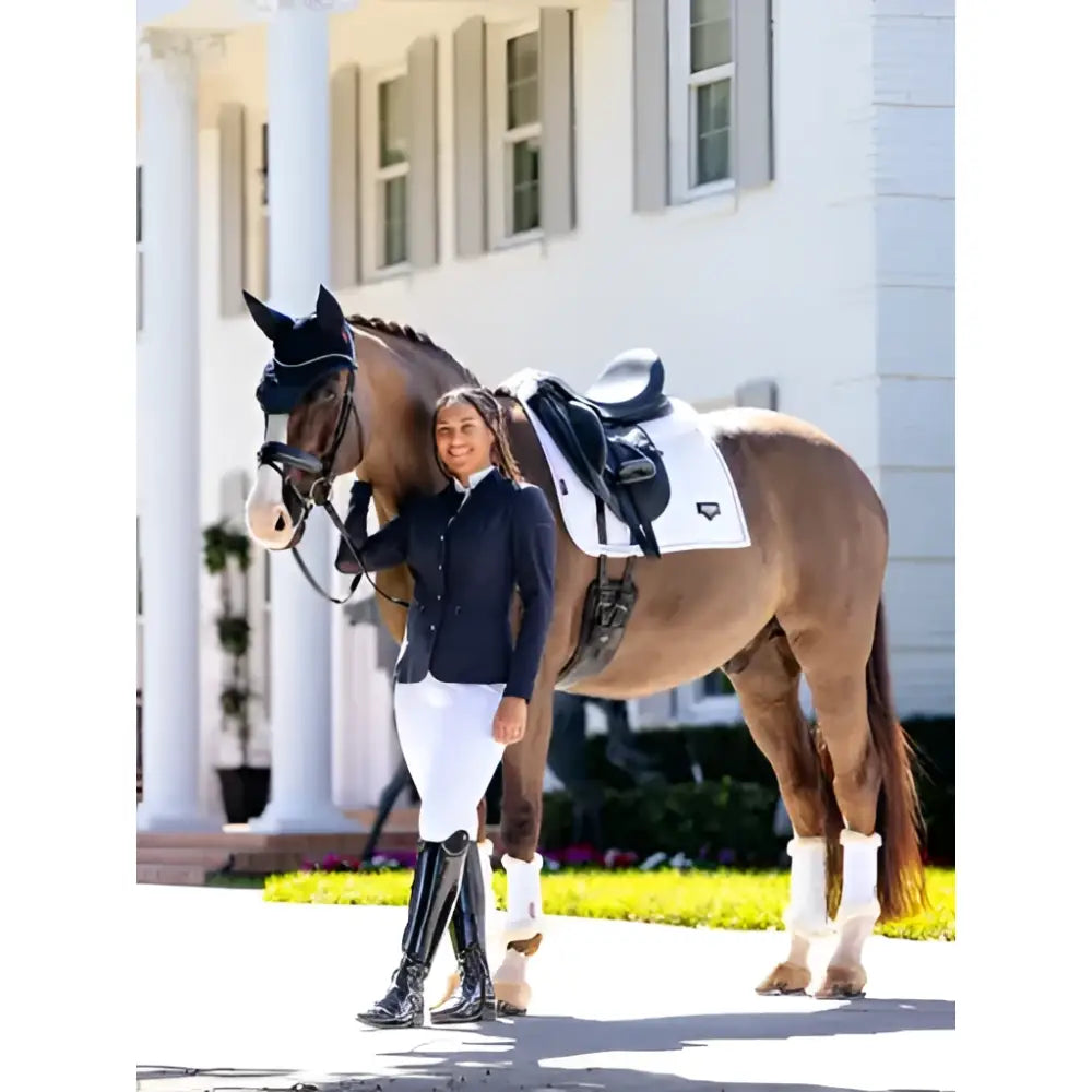 A sleek black horse stands with its rider wearing elegant gear beside a white lemieux puissance suede dressage pad