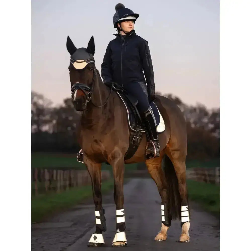 Dark brown horse wearing lemieux reflective black and white reach boots wrap protecting the horse’s heel