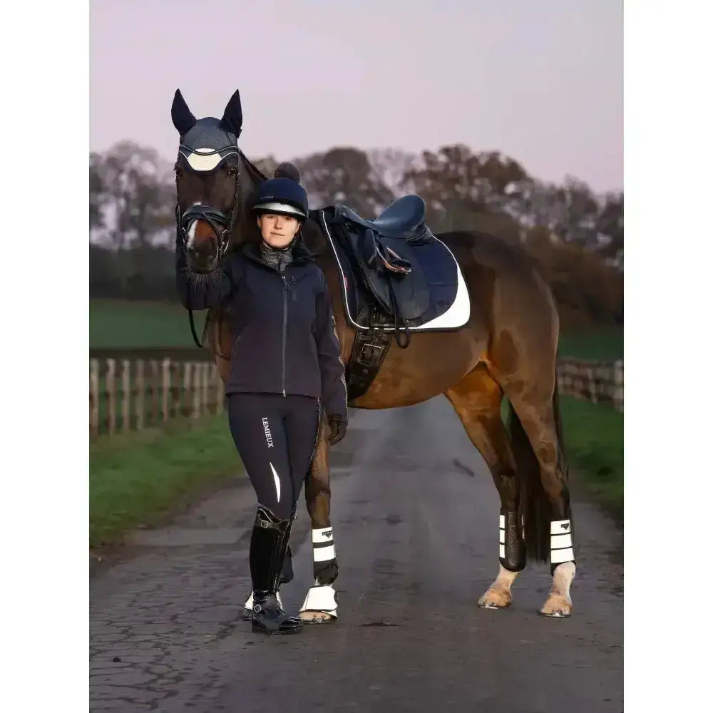 Dark brown horse wearing black headgear and navy blue lemieux reflective suede dressage saddle pad