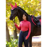 A horse wearing lemieux sara snood base layer cranberry in vibrant red with padded ear flaps and matching bridle straps