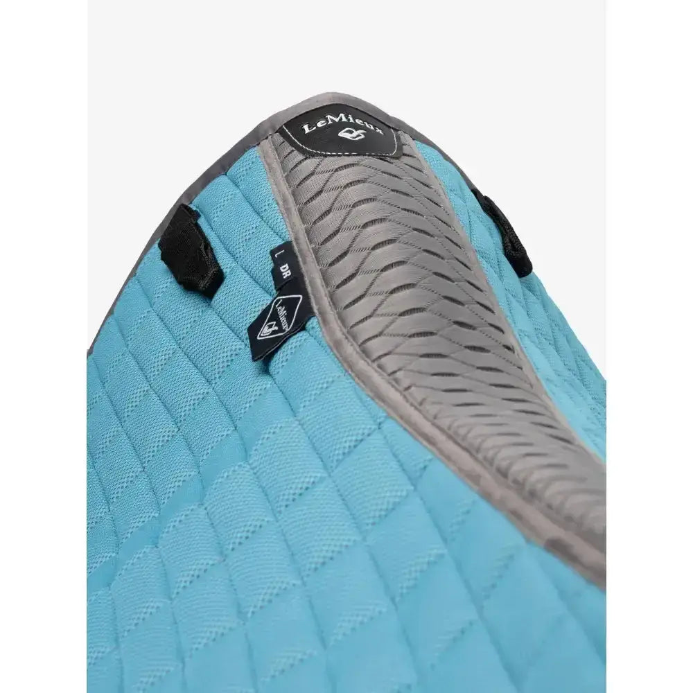 Light blue quilted lemieux self-cool dressage square with gray textured padding and black brand tags for dressage use