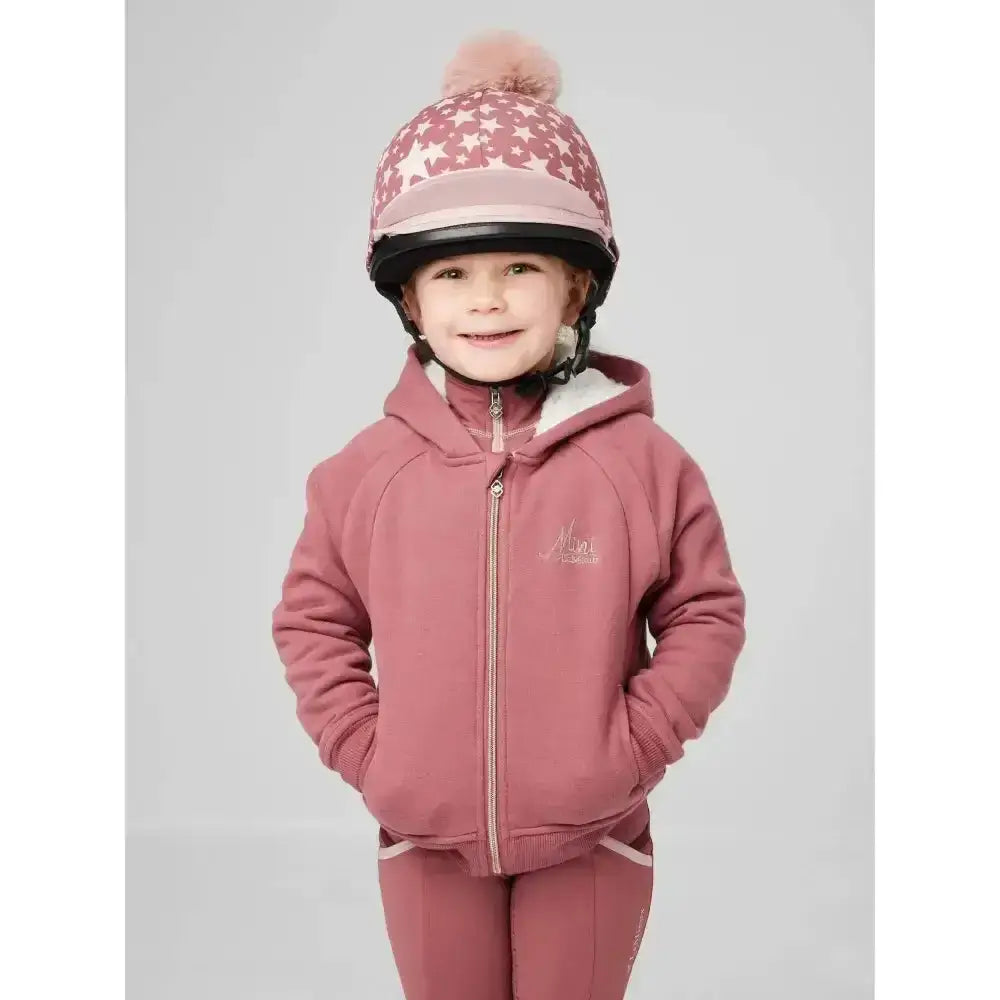A child wearing a pink star-patterned helmet and lemieux sherpa lined lily hoodie orchid with fluffy pom-pom on top